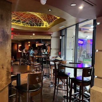 Warm-lit bar and high-top seating under a stained-glass ceiling feature at Iron Cactus San Antonio